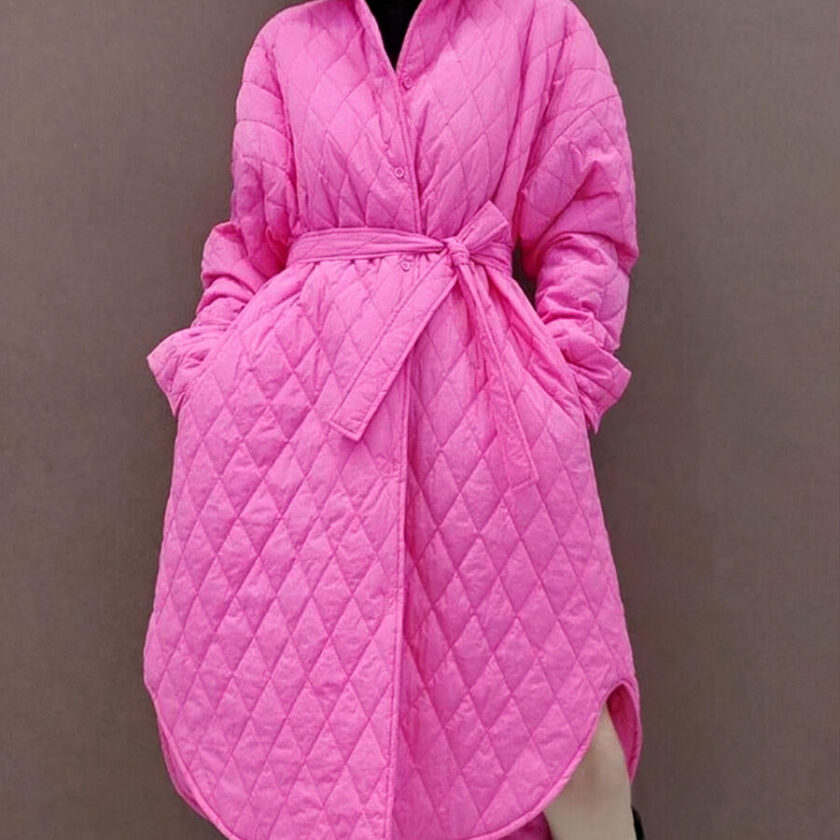 Wir sehen eine Frau, die eine fuchsiafarbene, gesteppte Daunenjacke mit Gürtel trägt. Die Jacke ist trapezförmig geschnitten.