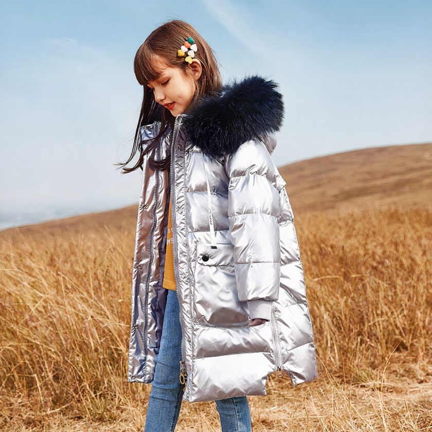 Lange graue Daunenjacke mit Pelzkapuze, die von einem dunkelhaarigen Teenager auf einem Feld getragen wird.