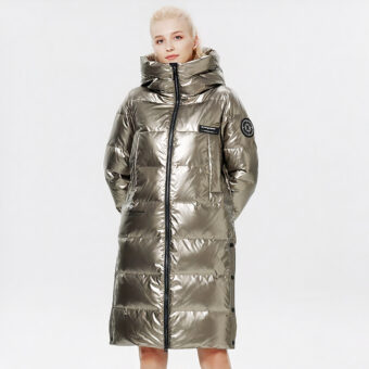 Frau, die eine lange goldene Daunenjacke auf grauem Hintergrund trägt.