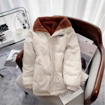 Sie sehen eine weiße Cordjacke für Herren, die mit braunem Fleece gefüttert ist. Sie liegt auf einem Sofa in einem maskulin eingerichteten Raum.
