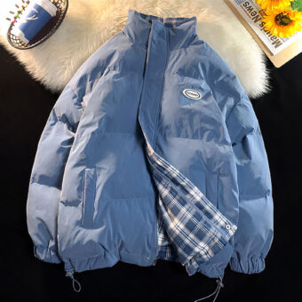 Das Foto wurde von oben aufgenommen: Sie sehen eine blaue Wendejacke mit einem blauen Karomuster. Sie liegt auf einem Teppich in Schaffelloptik.