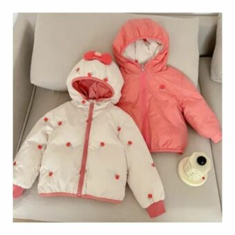 Reversible Daunenjacke für Mädchen in rosa, die auf einem beigefarbenen Sofa liegt.