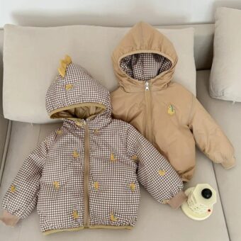Beidseitig tragbare Daunenjacke mit Panda- oder Dino-Karos für Kinder in der braunen Dino-Version, die auf einem beigen Sofa liegt.