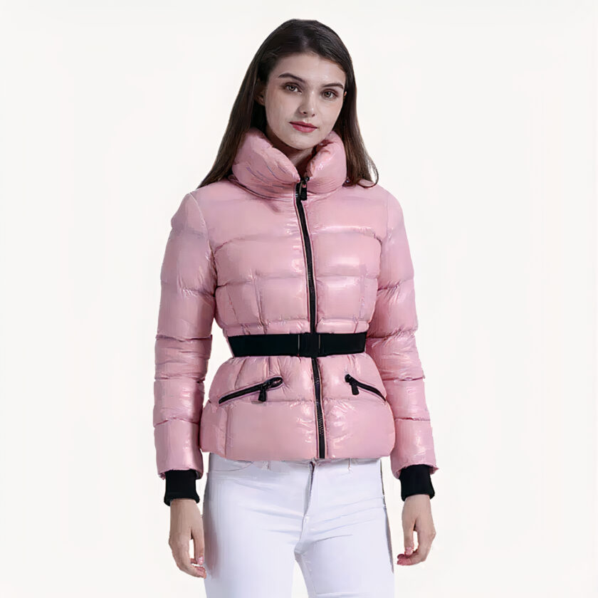 Brünette Frau, die eine rosa Daunenjacke mit einem schwarzen Gürtel und einer weißen Hose trägt