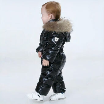 Schwarze Jumpsuit-Daunenjacke für Baby-Jungen, getragen von einem kleinen Jungen, der vor einem blauen Hintergrund läuft.
