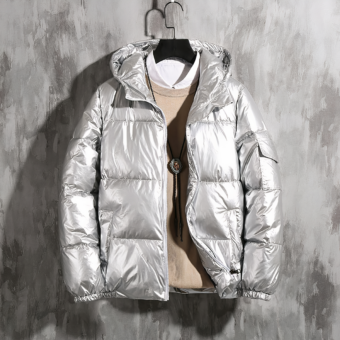 Foto einer silbernen Daunenjacke für Herren auf einem Kleiderbügel vor einer Wand aus gewachstem Beton. DIE Daunenjacke wird mit einem beigen Pullover und einem weißen Hemd getragen.
