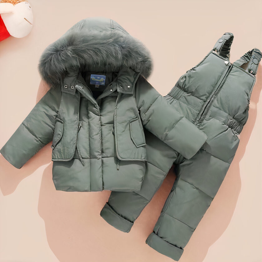 Winterjacke für Baby-Jungen in grün auf orangefarbenem Hintergrund. Ein kleines Plüschtier befindet sich in der oberen linken Ecke des Bildes.