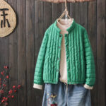 Grüne, blousonartige Daunenjacke, die an einem hängenden Bügel über einem Pullover und einer Jeans getragen wird.