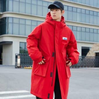 Bild eines Mannes, der eine rote halblange Daunenjacke und eine marineblaue Mütze trägt. Er steht auf der Straße und hat seine Hände in den Taschen der Daunenjacke.