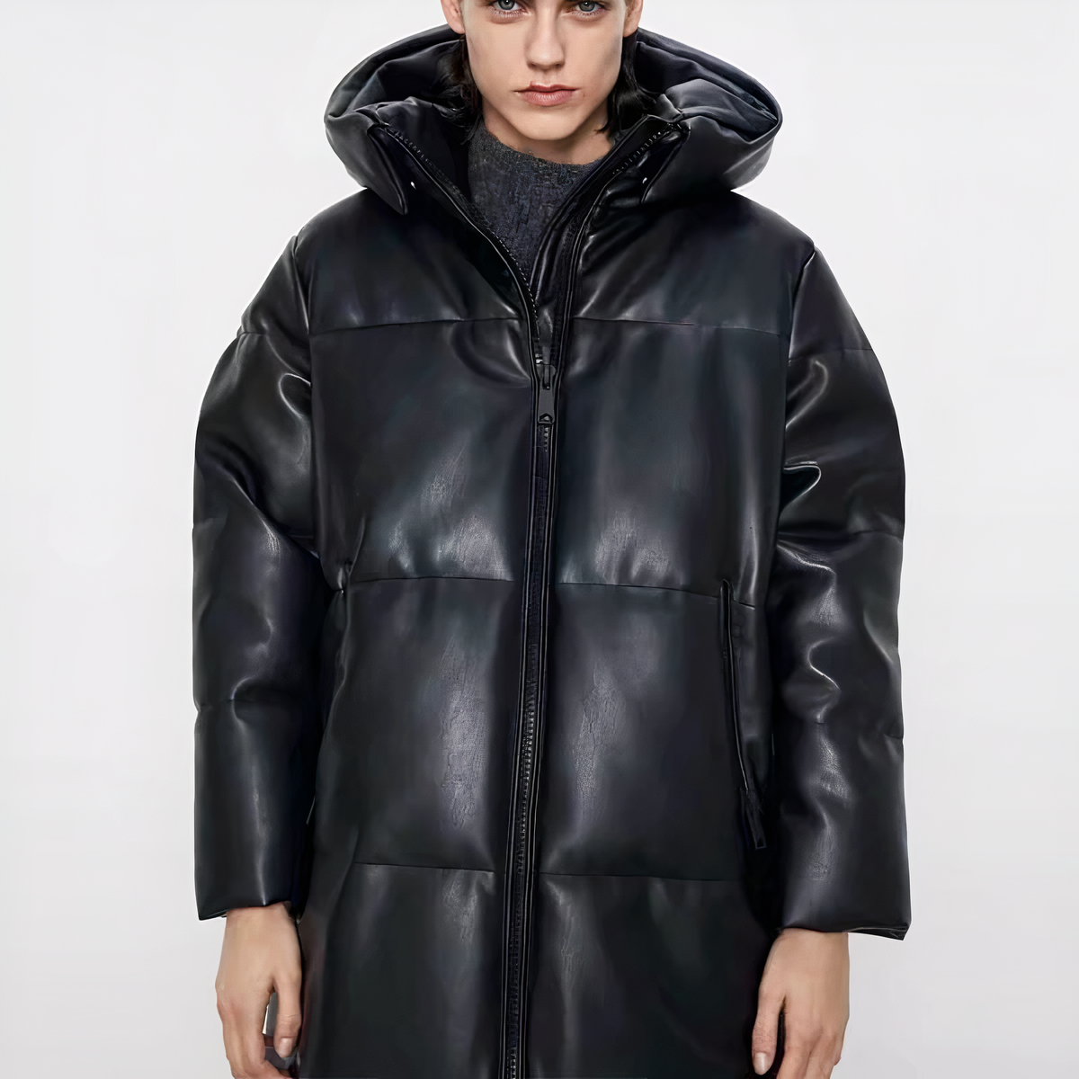 Wir sehen einen großen jungen Mann mit sehr blasser Haut, wahrscheinlich ein Model, der eine halblange Daunenjacke aus Kunstleder trägt. Er posiert vor einem weißen Hintergrund und lächelt nicht.