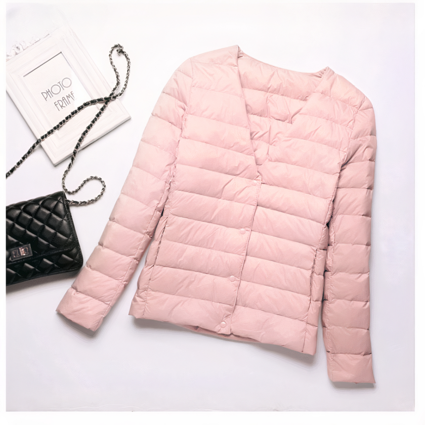 Kurze, dünne, rosafarbene Daunenjacke für eine Frau, die flach auf weißem Hintergrund präsentiert wird, mit einer Handtasche, die daneben liegt