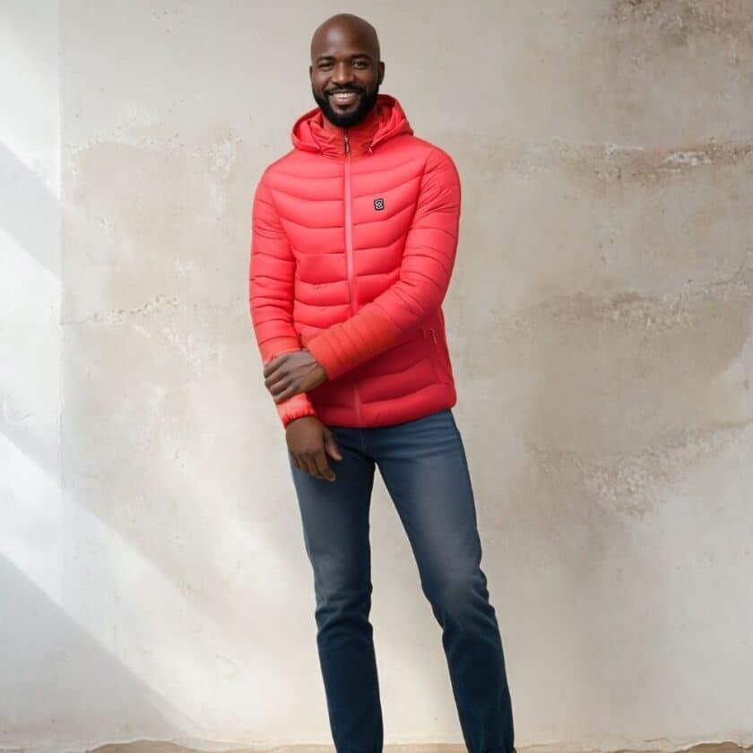 Rote beheizbare Daunenjacke, die von einem Mann getragen wird, auf einem betongrauen Hintergrund.