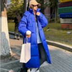 Foto einer Frau mit einer langen blauen Daunenjacke auf der Straße