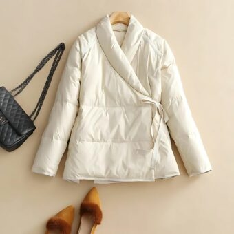 Kurze Damen-Daunenjacke mit Weste auf beigem Hintergrund. Eine schwarze Handtasche liegt daneben.