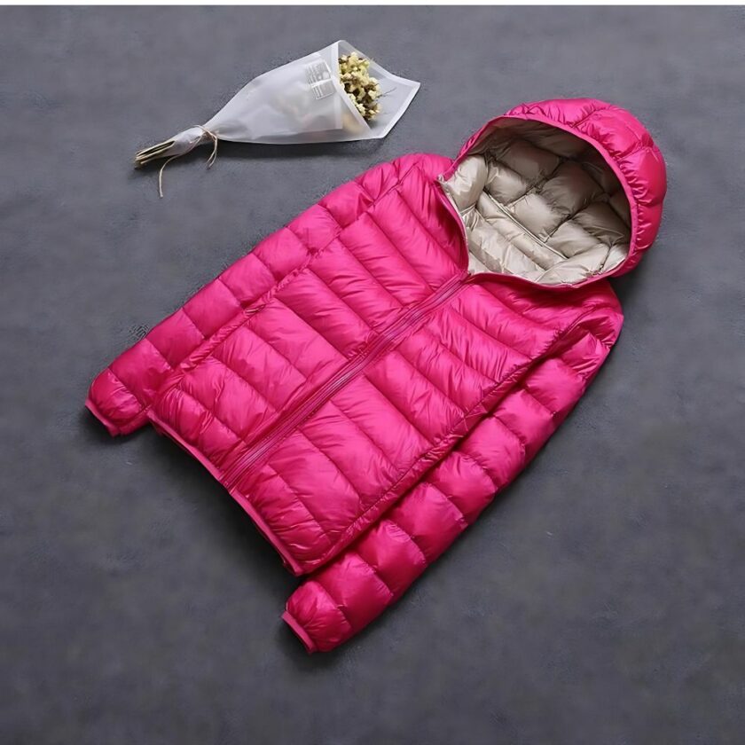 Große, wendbare Damen-Daunenjacke in Hellrosa, flach gelegt mit einer beigefarbenen Kapuze, begleitet von einem Blumenstrauß aus weißem Papier.