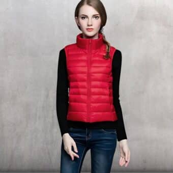 Rote Daunenjacke, die von einer jungen blonden Frau getragen wird, die unter der Daunenjacke einen schwarzen Pullover und eine Jeans in Rohkostfarbe trägt.