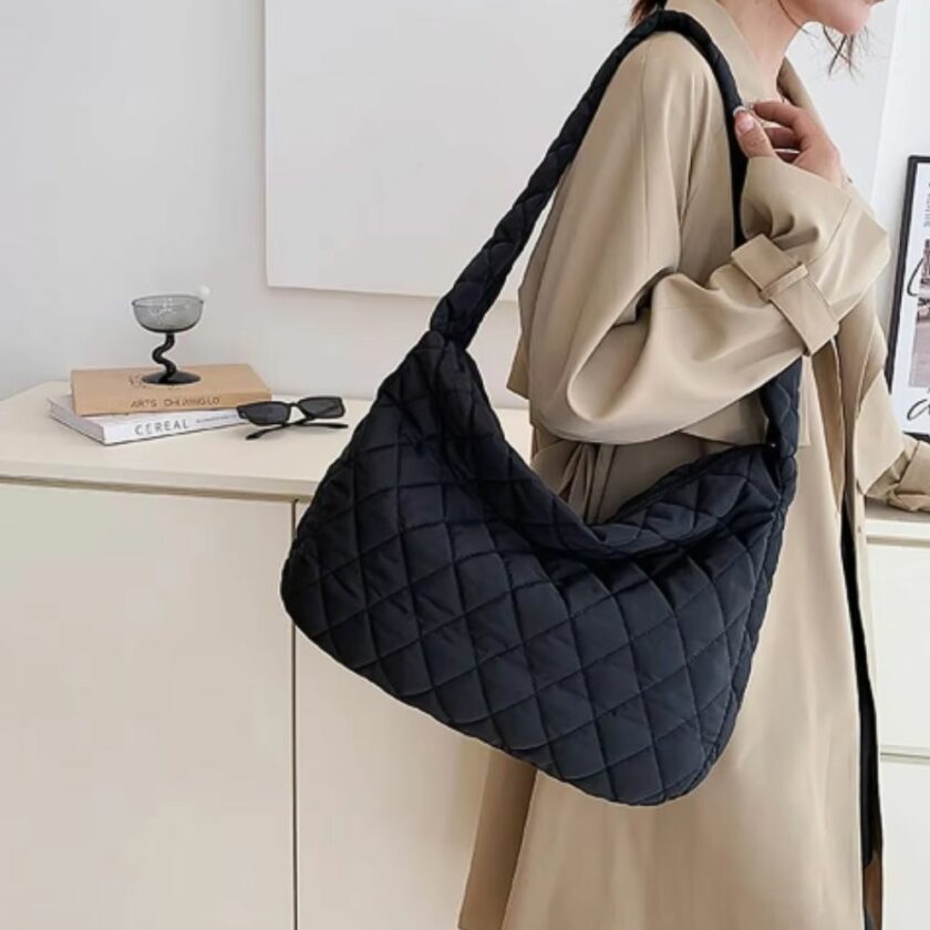 sie sehen eine Frau mit einem beigen Mantel, die eine schwarze Handtasche mit Daunenjacke trägt